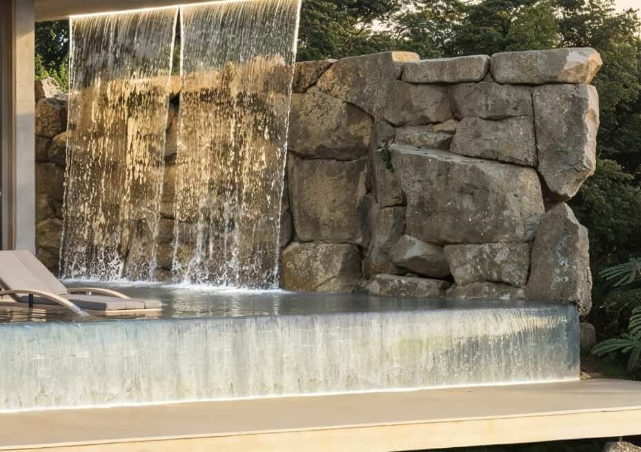 The pool's stone waterfall: sheets of water falling across a boulder wall into the overflow channel beside the deck.